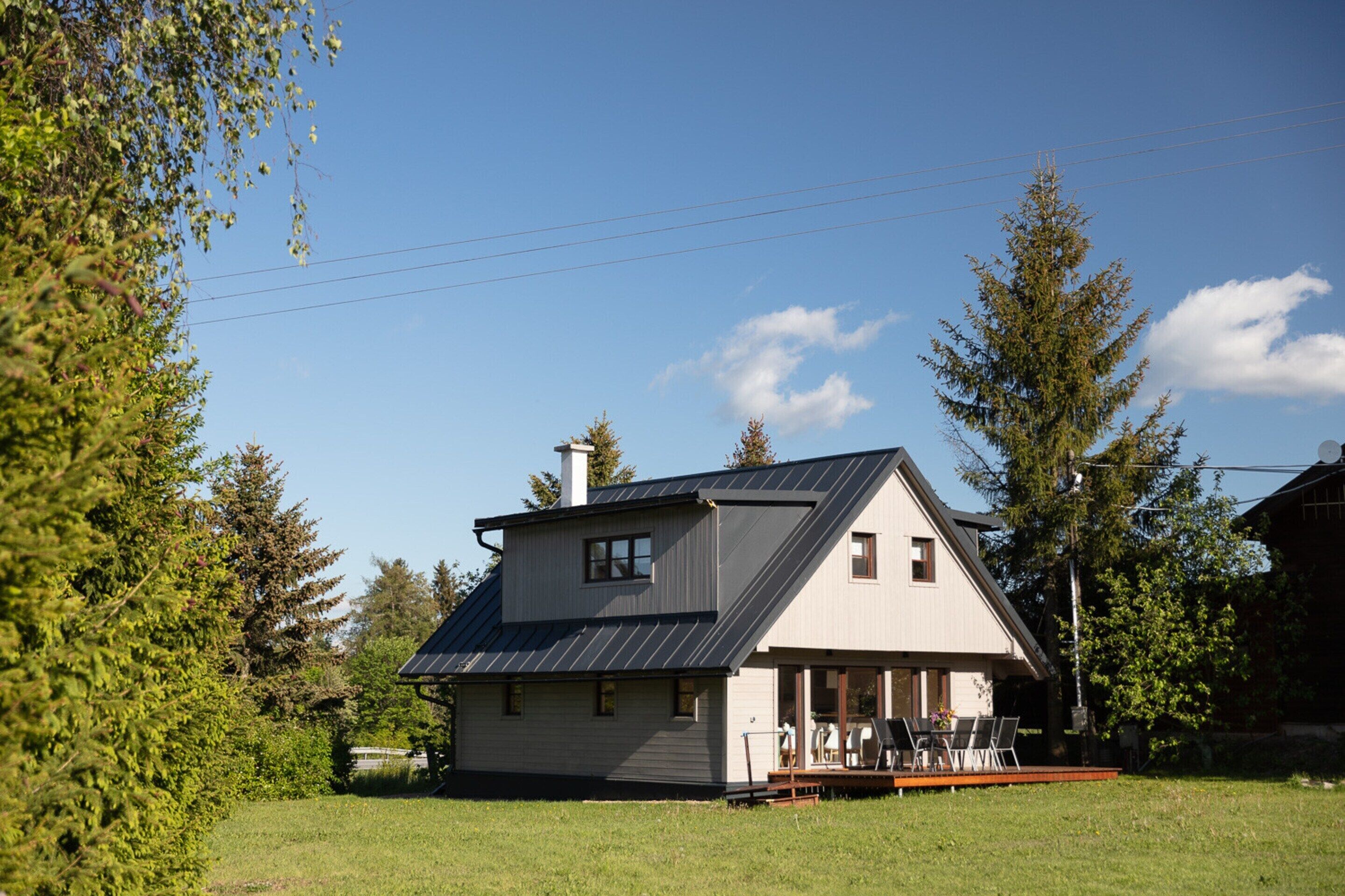 Une maison à deux étages avec un toit en pente, un porche à l’avant avec des chaises et une petite terrasse.