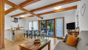 A spacious living area with a wooden ceiling, a grey sofa, a wooden coffee table, and a dining area with chairs and a table.
