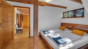 A bedroom with a wooden ceiling, a bed with two pillows, a chair, and a window with a view of trees.