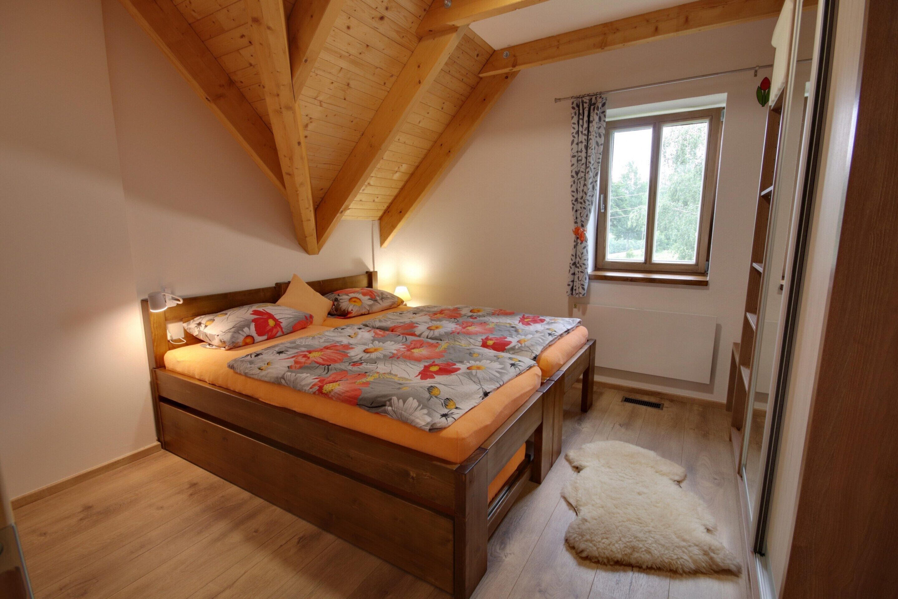 Ein Schlafzimmer mit Holzboden, einem Bett mit Blumenmuster-Bettwäsche, einem Fenster mit Vorhängen und einem weißen Teppich.