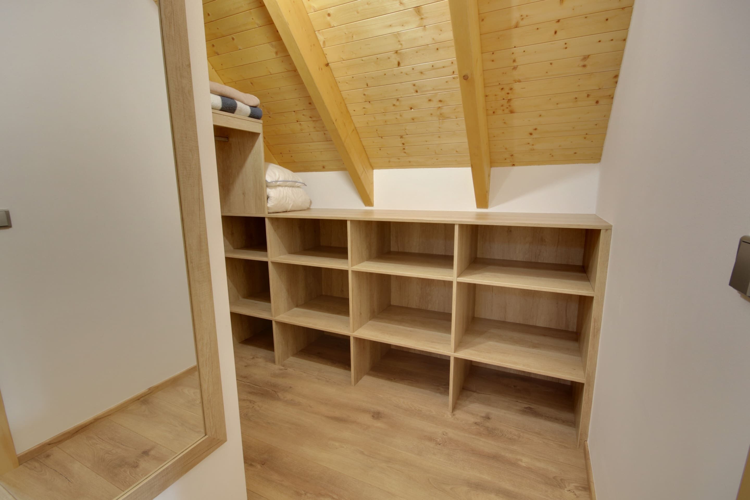 A room with a sloped ceiling, wooden beams, and built-in shelving.