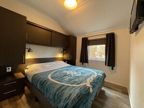 Ein Schlafzimmer mit einem Bett, einem dunklen Holzschrank, Nachttischlampen und einem Fenster mit Vorhängen.