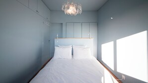 A bedroom with a bed, a hanging light fixture, and a window.
