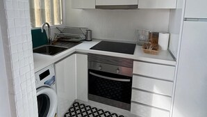 A compact kitchen with a washing machine, a sink, a stove, and a small window with curtains.