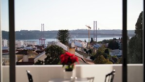 A view from a balcony with a table and chairs, overlooking a cityscape with buildings, a bridge, and a body of water.