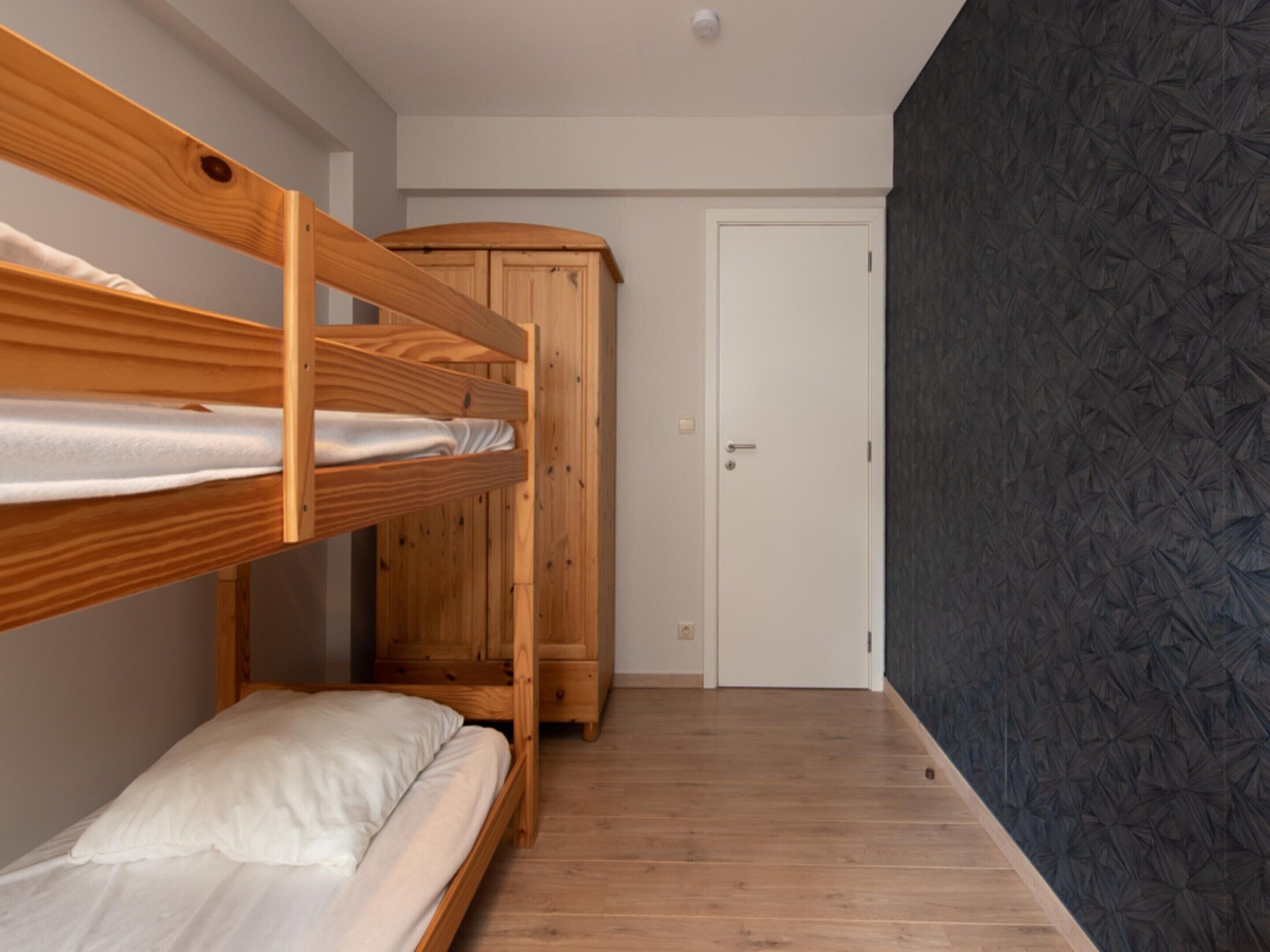 Een kamer met een stapelbed, een houten garderobe en een deur.