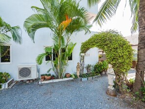 A courtyard with a white building, palm trees, and a statue. - Lemon House apartment (Koh Samui)