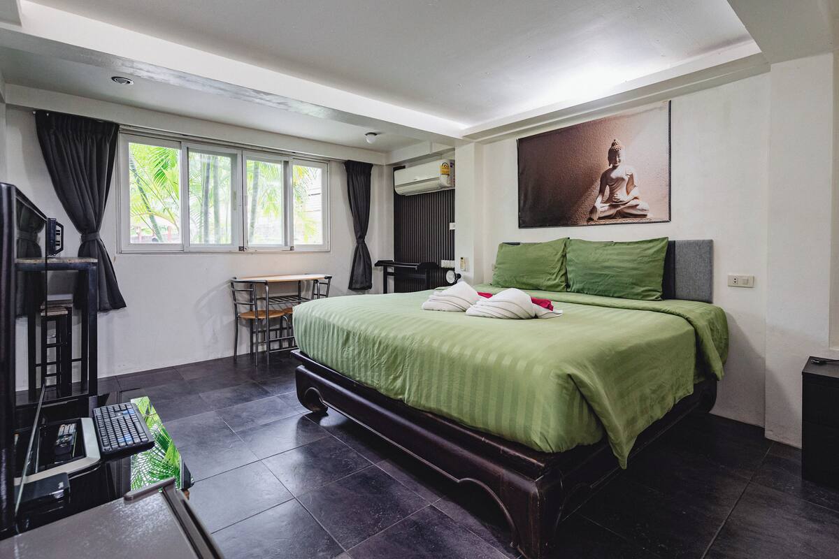 Habitación de hotel con una cama grande, un escritorio, una silla y un ventanal con cortinas.