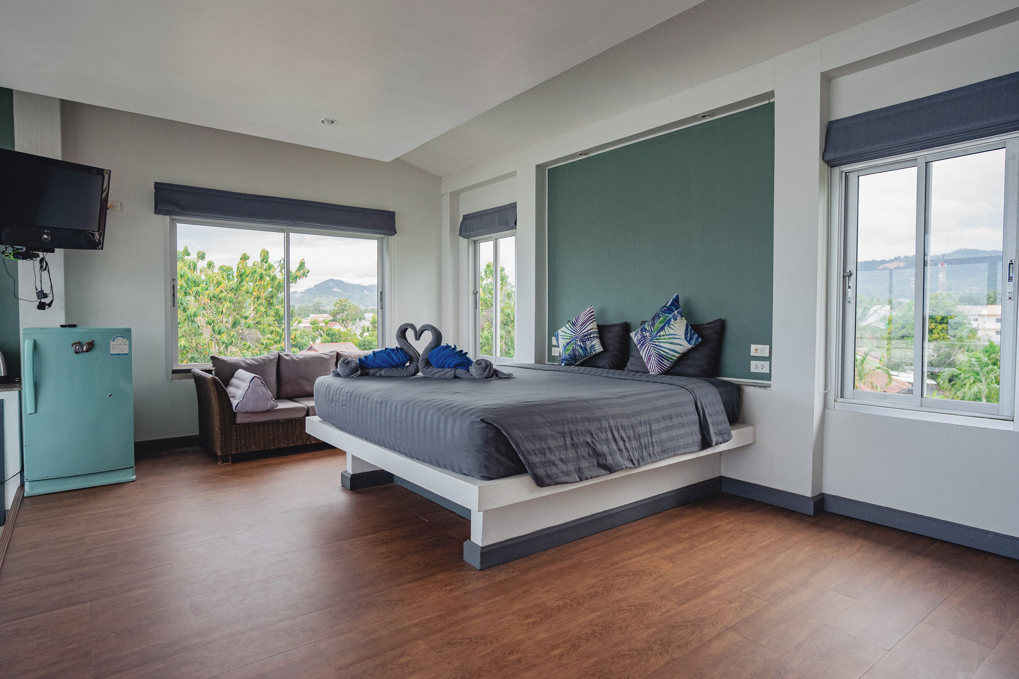 Quarto moderno com cama, sofá, televisão e janelas amplas.