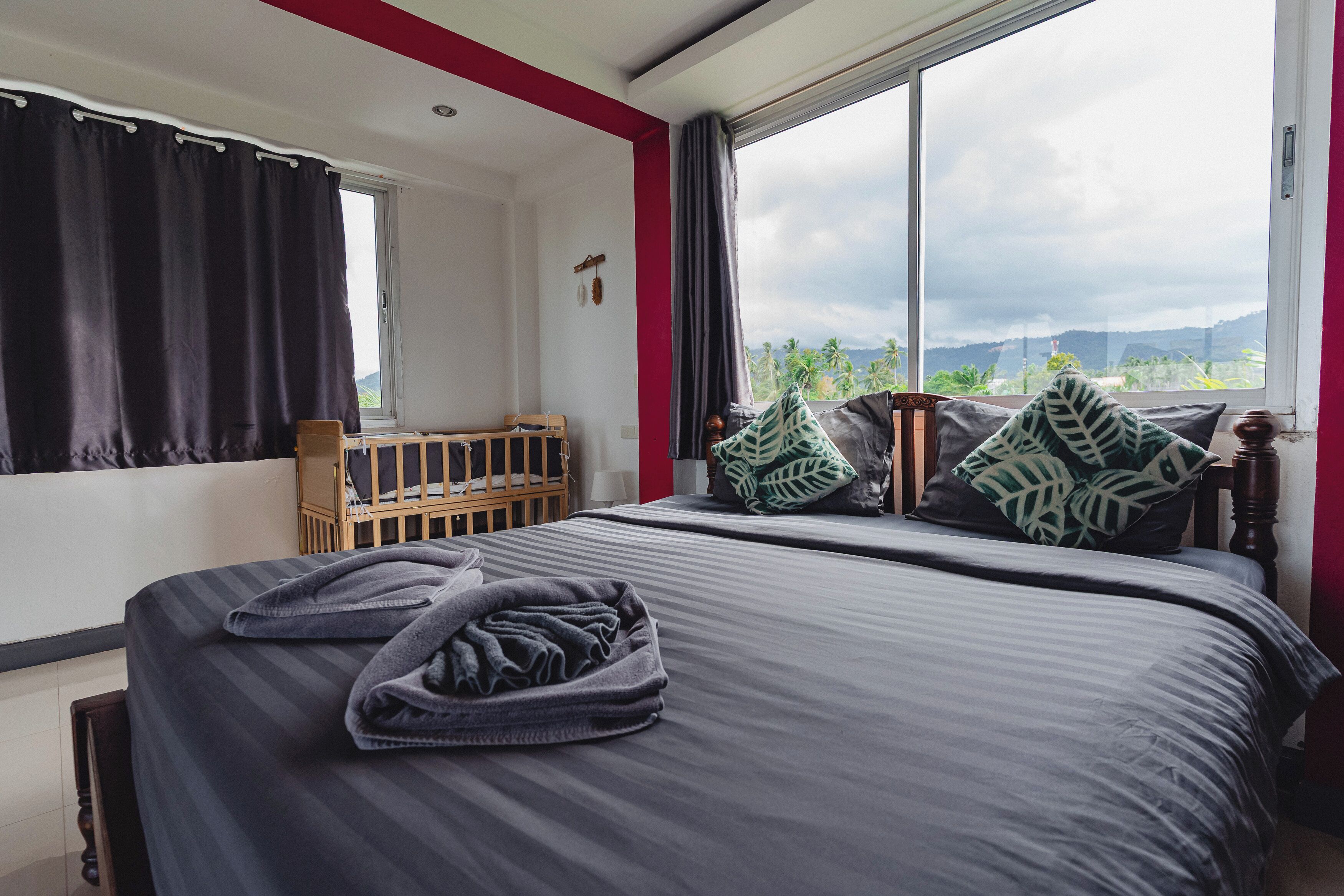 A bedroom with a large bed, a wooden crib, and a view of the mountains through a window.