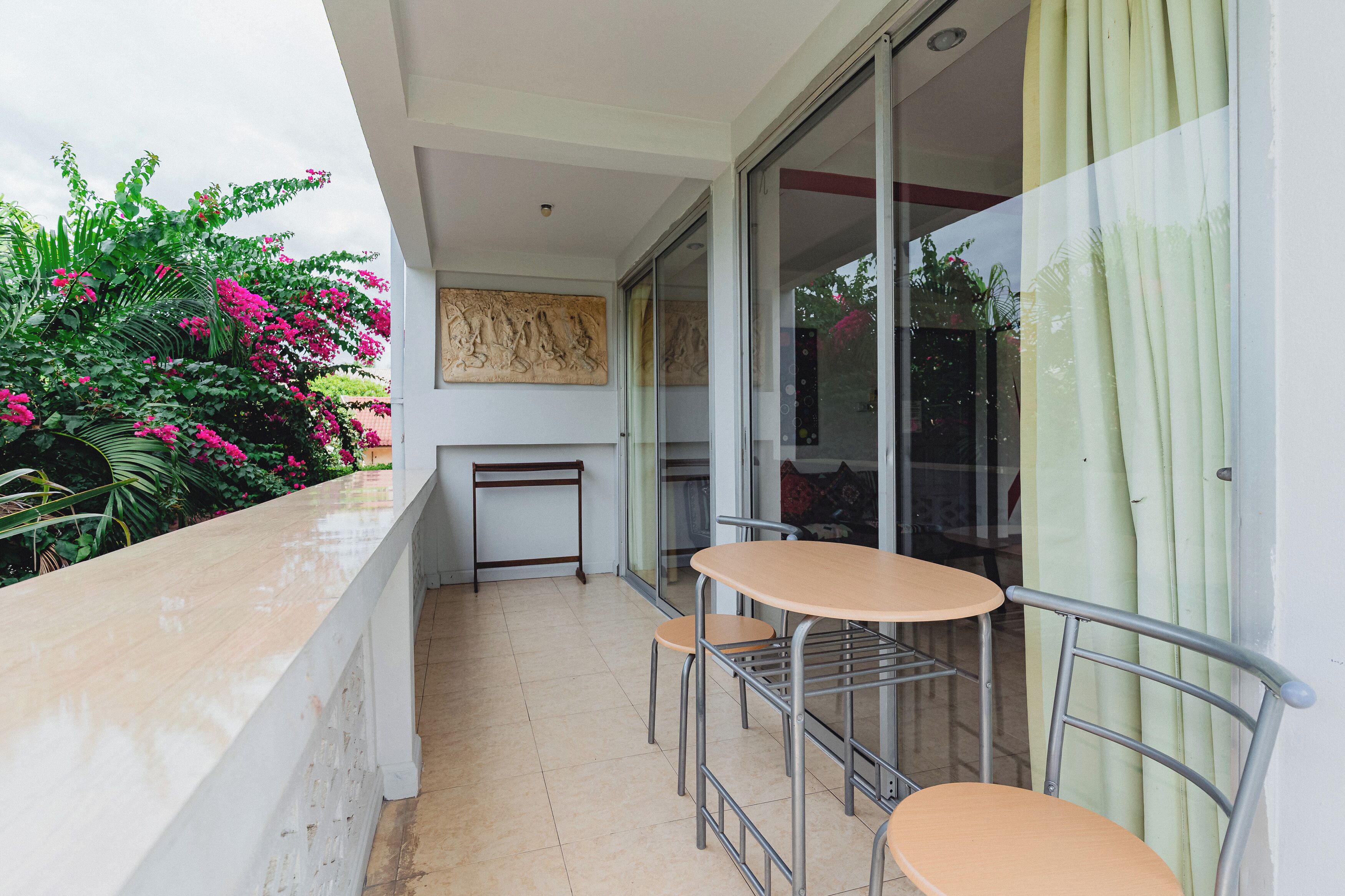 Varanda com mesa e cadeiras, porta de correr de vidro e vista para um jardim com flores cor-de-rosa.