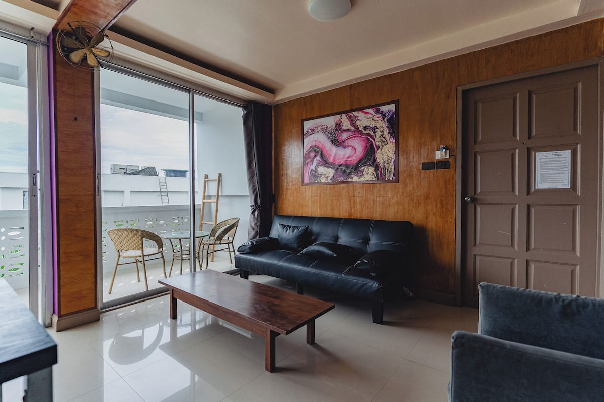 Una sala de estar moderna con un sofá de cuero negro, una mesa de centro de madera y un amplio ventanal con vistas a la ciudad.