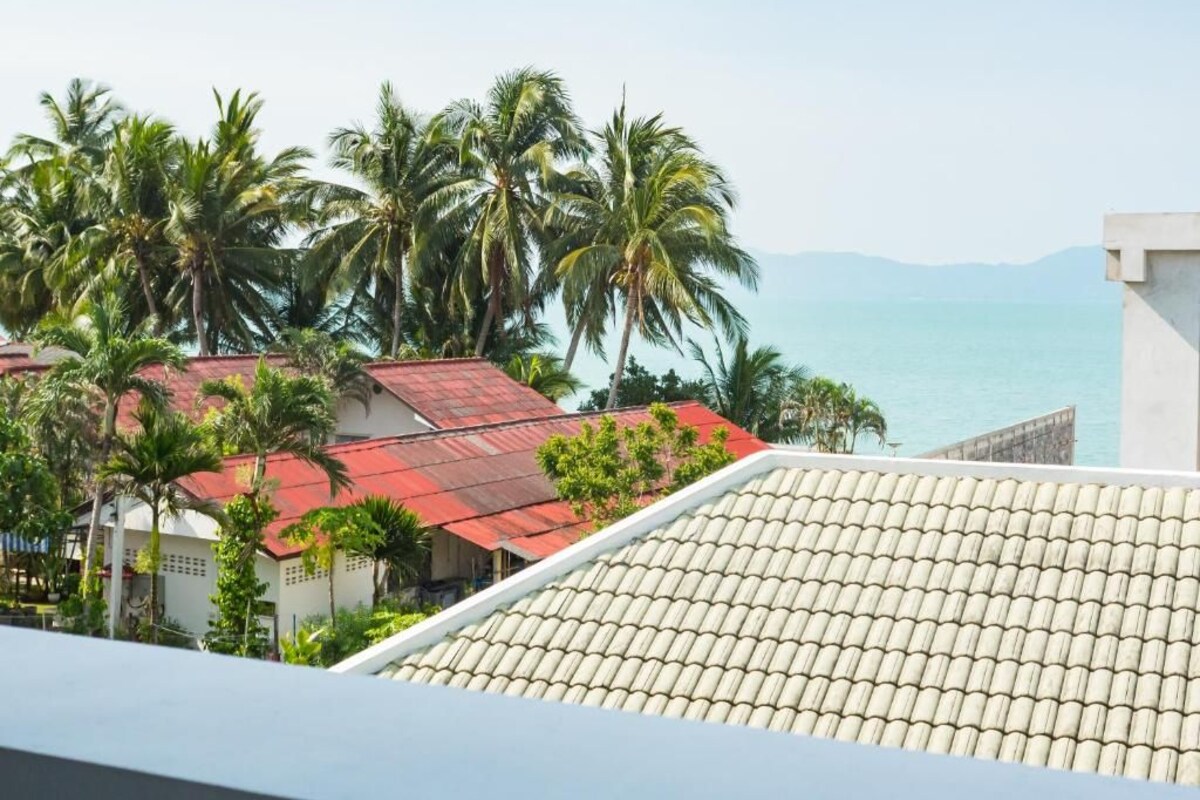 A coastal view with a tiled roof, palm trees, and a clear sky.