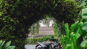 A motorbike parked under a lush green archway in a garden area. - Lemon House apartment (Koh Samui)