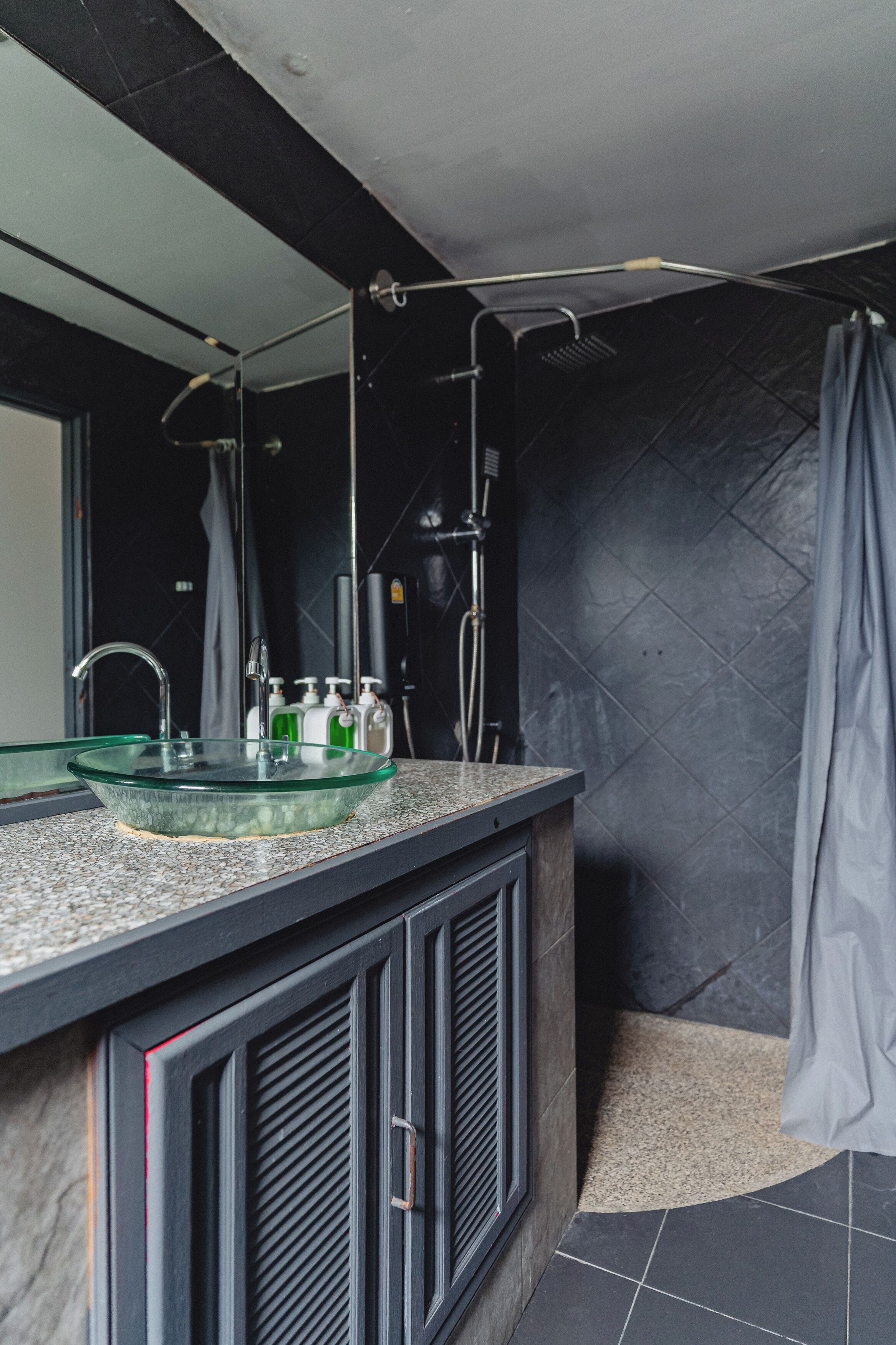 Une salle de bain moderne avec un lavabo en verre, des meubles noirs et un espace douche.