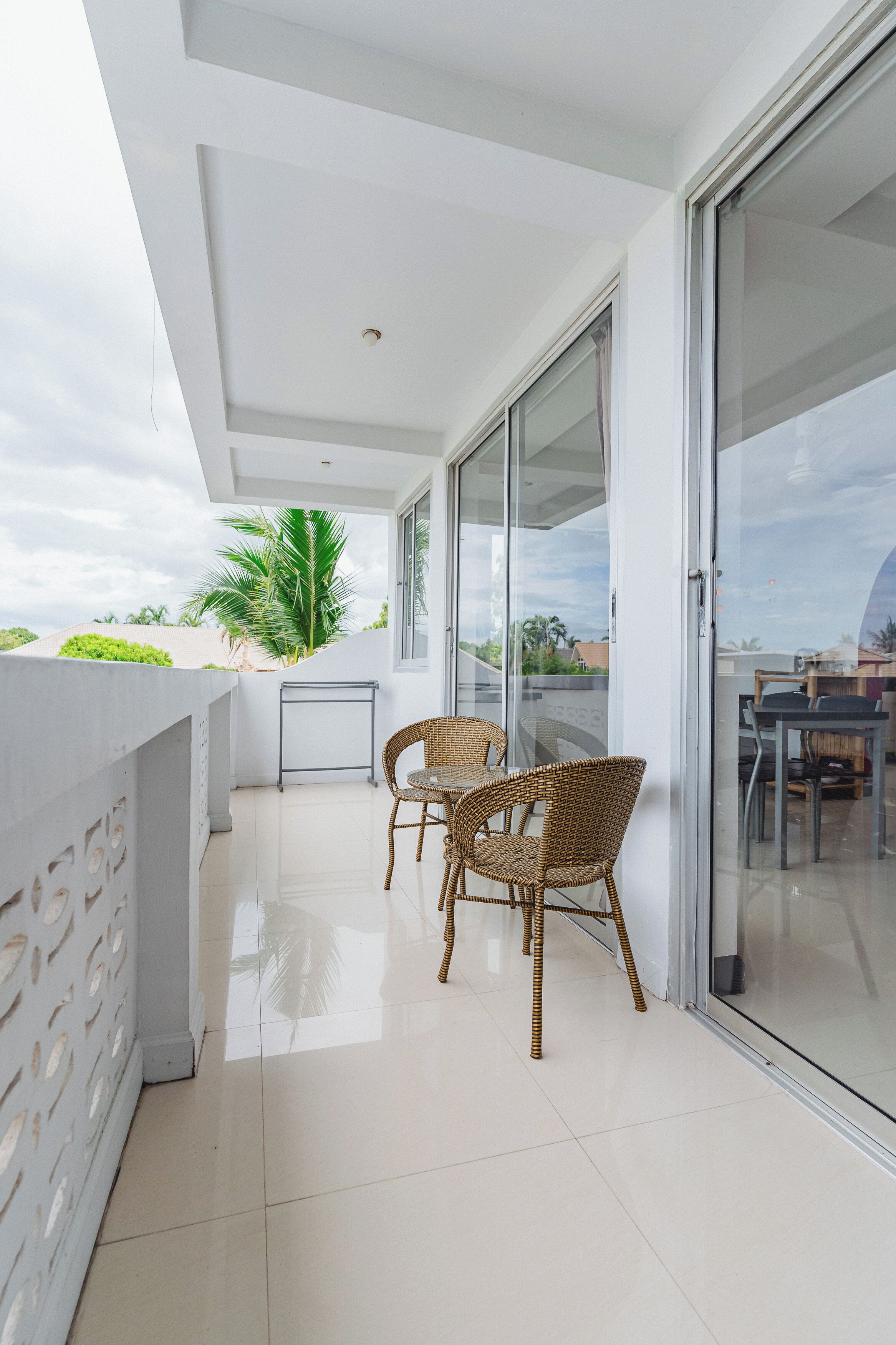 En balkon med to fletstole og et bord, en glasdør samt udsigt til palmer og bygninger.