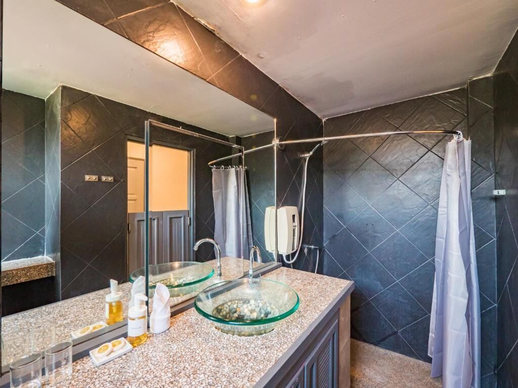 Un baño moderno con un lavabo de vidrio, ducha y paredes de azulejos oscuros.