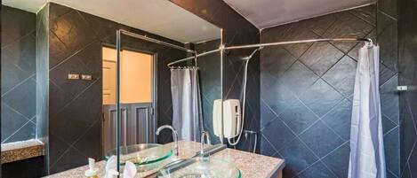 Un baño moderno con un lavabo de vidrio, ducha y paredes de azulejos oscuros.