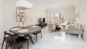 Ein modernes Wohnzimmer mit einem runden Esstisch, dunklen Stühlen, einer Couch und einem Fernseher.