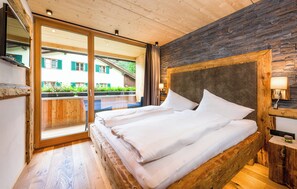 A wooden-framed bed with white bedding in a room with a stone wall and a large window. - Erholungswelt Lechrefugium (Steeg)