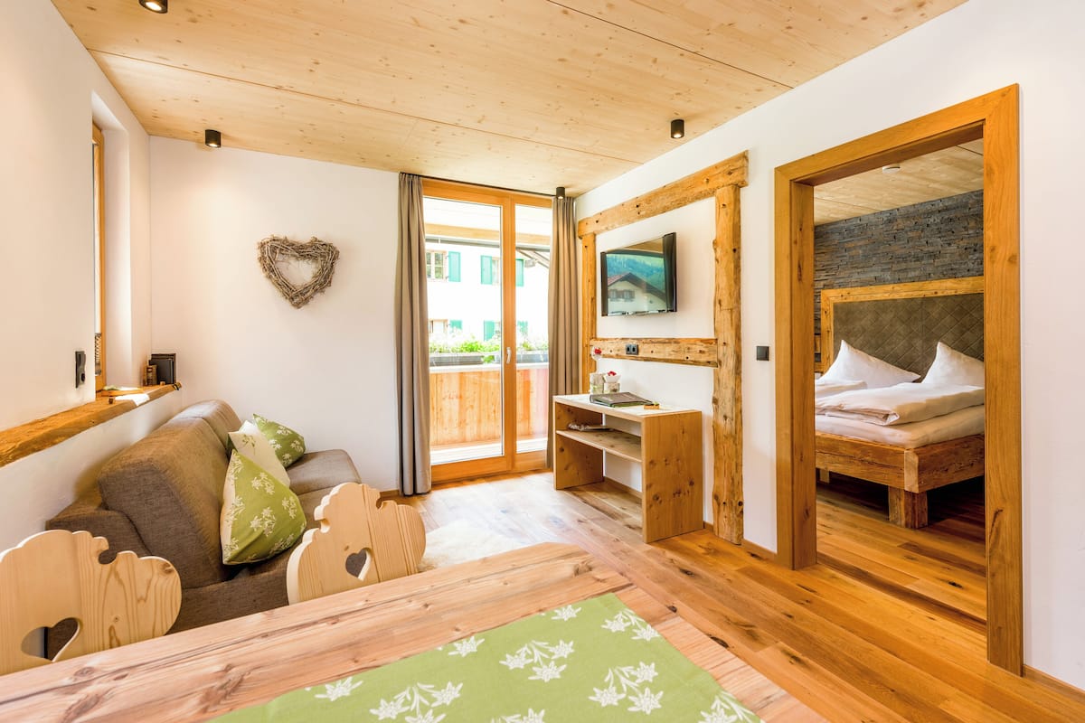 Une pièce chaleureuse avec un plafond en bois, un canapé agrémenté de coussins, une petite table, un lit avec des oreillers et un téléviseur fixé au mur.