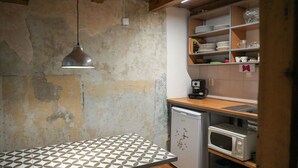 Une cuisine compacte avec une table en bois, un réfrigérateur, un four à micro-ondes et des étagères contenant de la vaisselle et une machine à café.