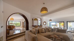 Un salon spacieux avec un grand canapé d’angle, une table basse en bois et un coin repas comprenant une table et des chaises en bois.