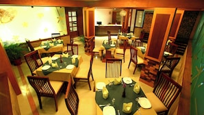 A dining area with multiple tables and chairs, a reception desk, and a potted plant. - Hotel Pearl Palace (Kanayannur)