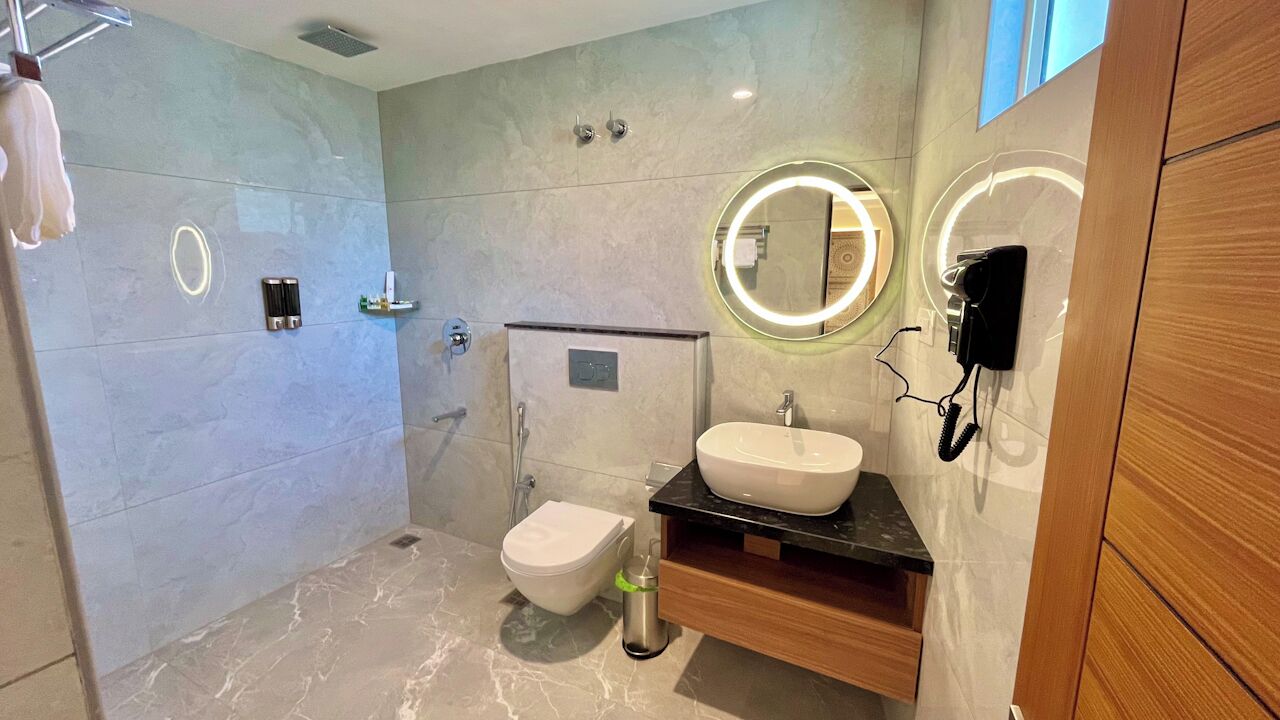 A modern bathroom with a marble floor, a white toilet, a sink with a mirror, and a handheld showerhead.
