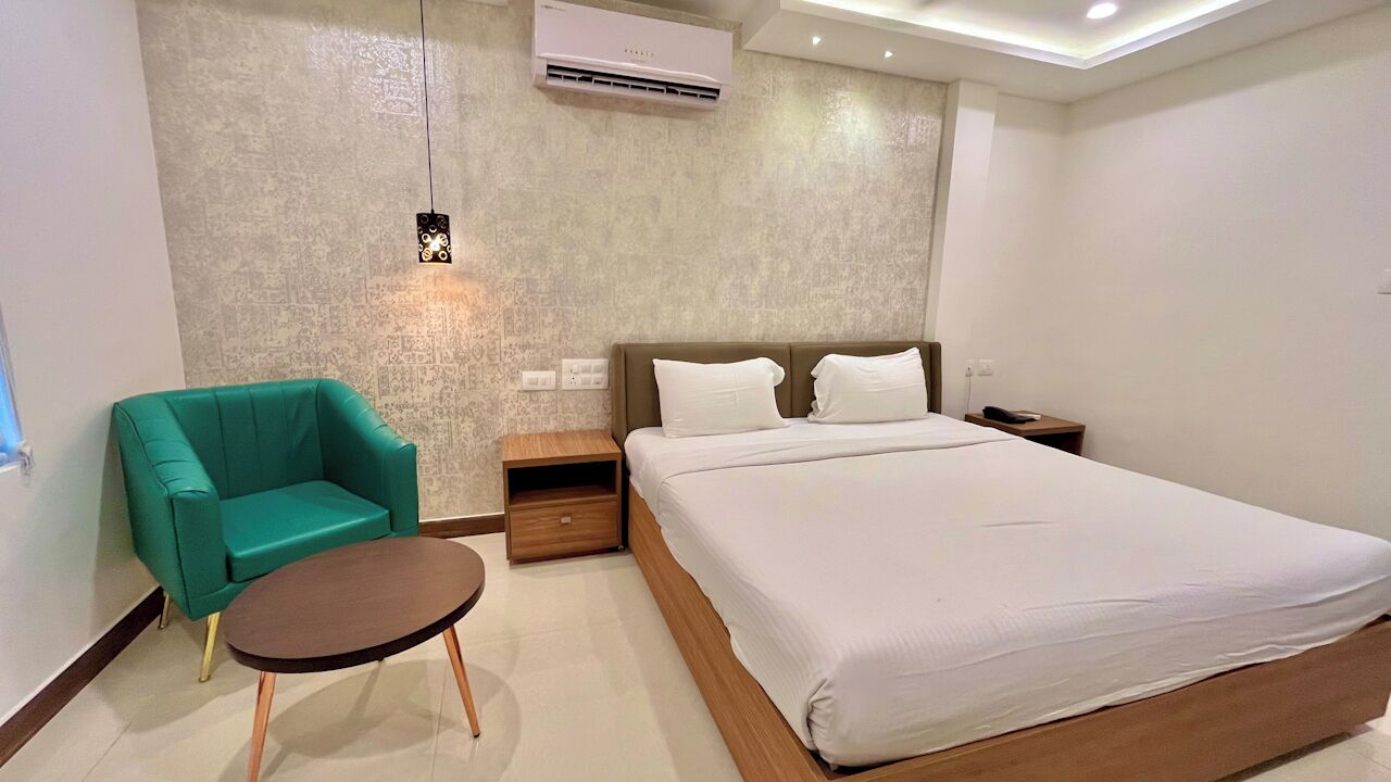 A modern hotel room with a large bed, a green armchair, a small table, and a nightstand.