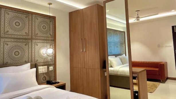A modern hotel room with a large bed, a wooden wardrobe, a bedside table, and a mirror. - Hotel Pearl Palace (Kanayannur)