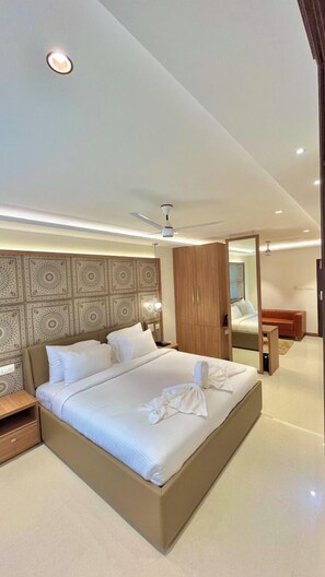 Une chambre d’hôtel moderne avec un grand lit, un ventilateur de plafond et une armoire en bois.