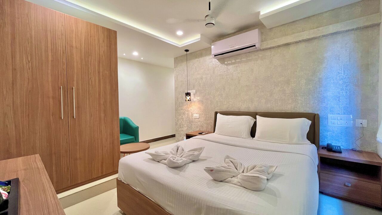 A modern hotel room with a large bed, a wooden wardrobe, a small round table, and a green chair.