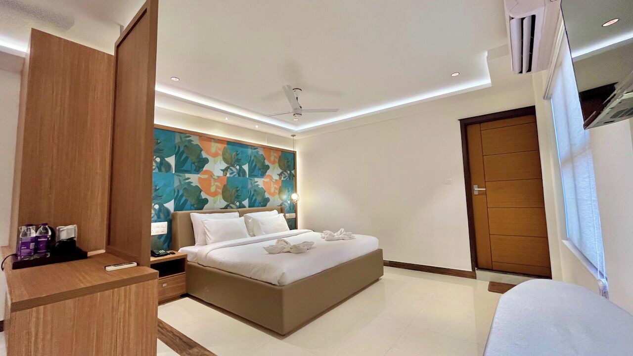 Une chambre d’hôtel moderne avec un grand lit, une armoire en bois, une table de chevet, un tableau au mur et une porte.