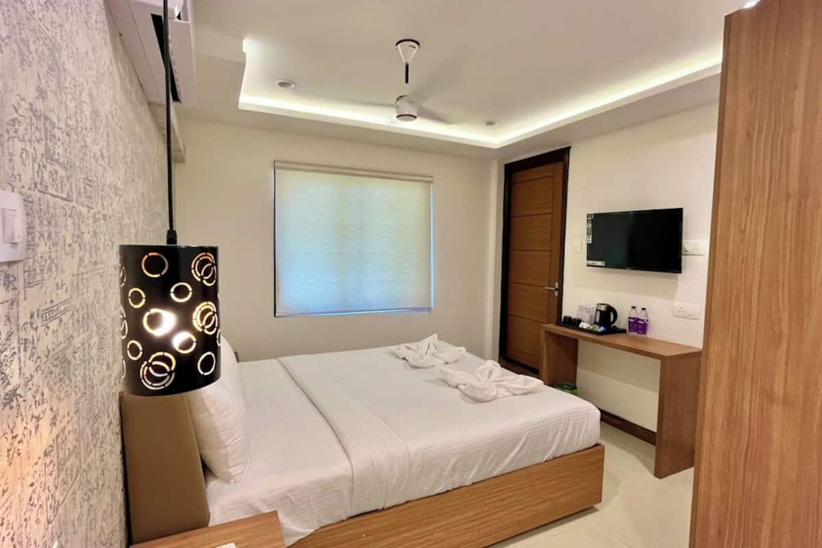 Een moderne slaapkamer met een bed, nachtkastje, televisie en raam met zonwering.
