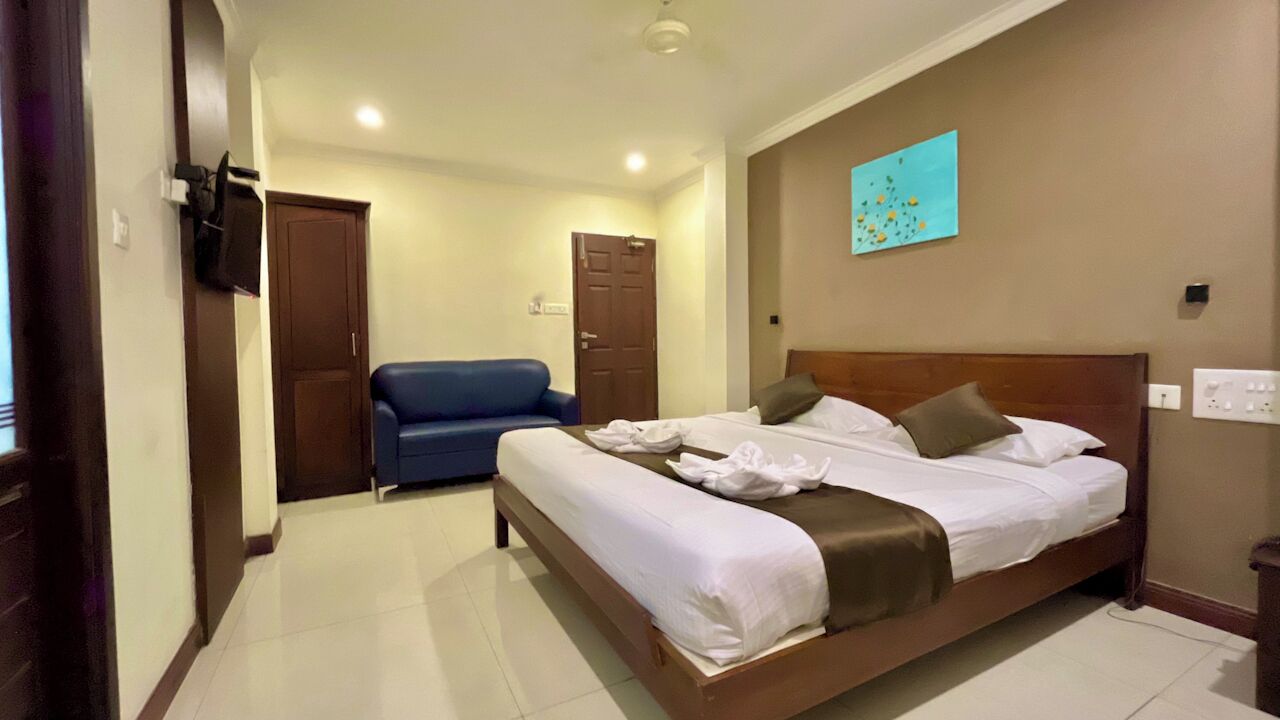 Une chambre d’hôtel avec un lit, un canapé bleu, une tête de lit en bois et une œuvre d’art accrochée au mur.