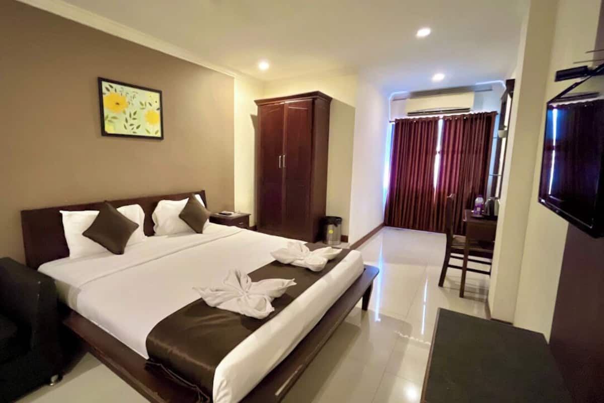 Een hotelkamer met een groot bed, een kledingkast, een bureau, een stoel en een televisie.