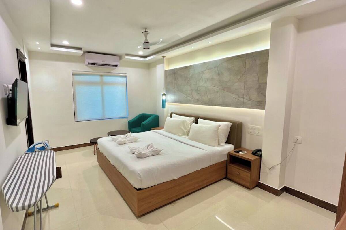 Een moderne hotelkamer met een groot bed, een nachtkastje, een stoel, een flatscreen televisie aan de muur en een raam met jaloezieën.