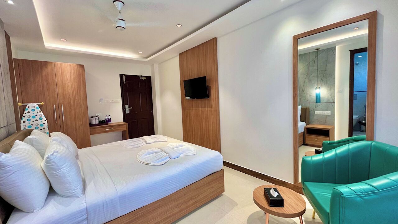 A modern hotel room with a large bed, a green sofa, a TV mounted on the wall, and a mirror reflecting the bathroom.