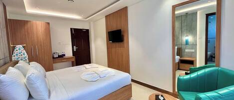 A modern hotel room with a large bed, a green sofa, a TV mounted on the wall, and a mirror reflecting the bathroom.