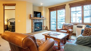 A living room with a fireplace, leather chairs, a sofa, and large windows.