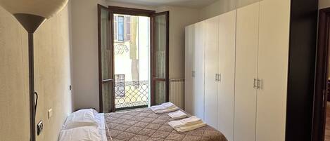 Un dormitorio con cama, armario, escritorio y ventana con vistas al exterior.