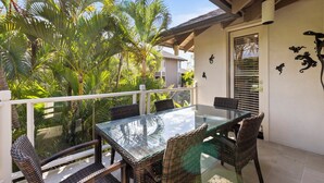 An outdoor balcony with a glass table and wicker chairs, surrounded by lush greenery and a white railing. - NEWLY REMODELED-QUIET LOCATION-AC-WELL EQUIPPED-METICULOUS CLEANING (Wailea)