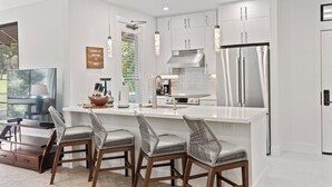 A modern kitchen with white cabinetry, a stainless steel refrigerator, and a central island with bar stools. - NEWLY REMODELED-QUIET LOCATION-AC-WELL EQUIPPED-METICULOUS CLEANING (Wailea)