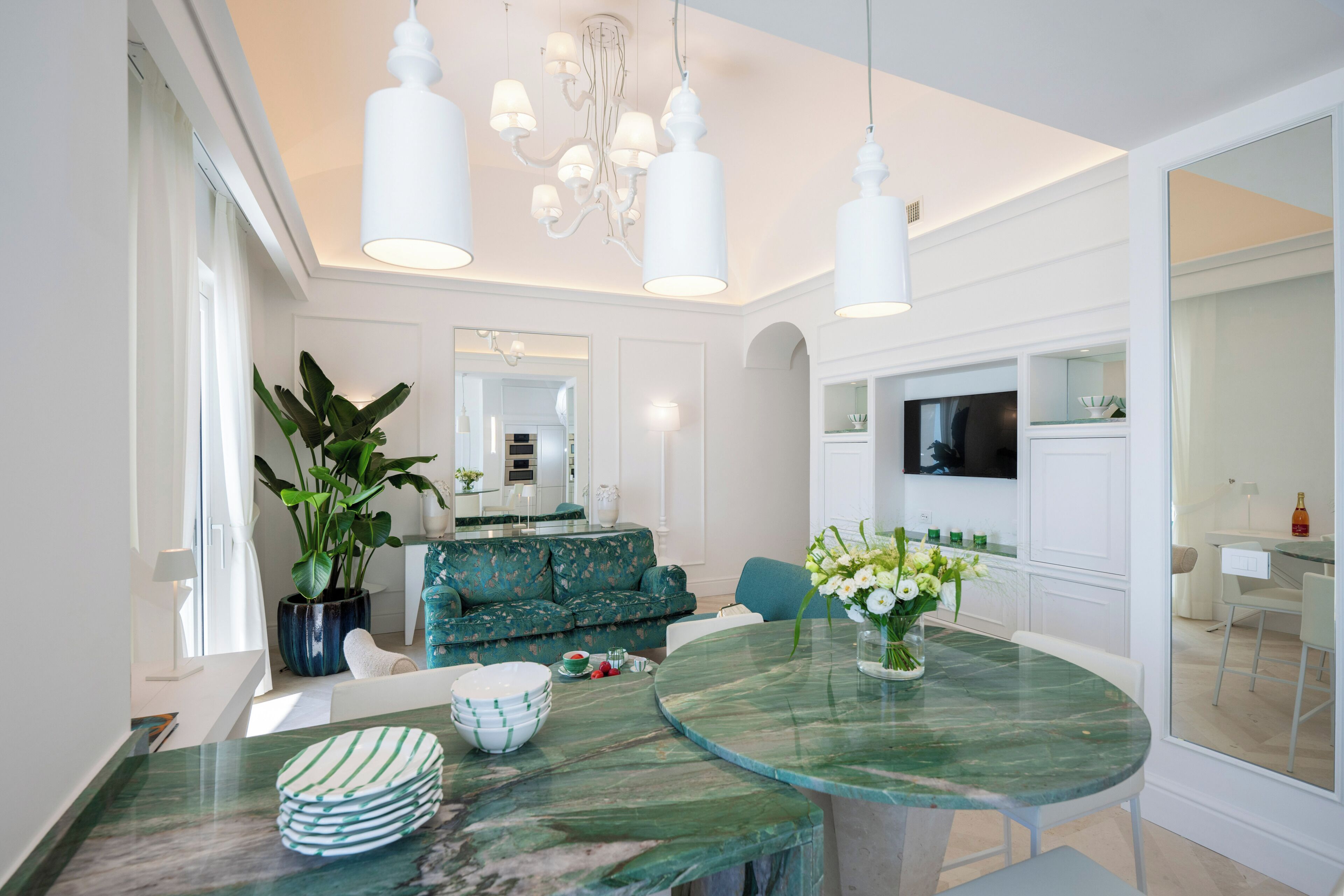 A modern dining area with a round glass table, white chairs, and a green sofa.