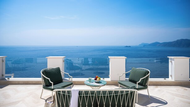 A balcony with two chairs and a table, overlooking a large body of water and distant land.