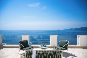 Un balcon avec deux chaises et une table, d’où l’on peut admirer une vaste étendue d’eau et une terre lointaine.