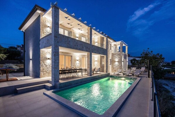 Une maison à deux étages dotée d’une piscine, d’un espace extérieur aménagé et de murs en pierre.