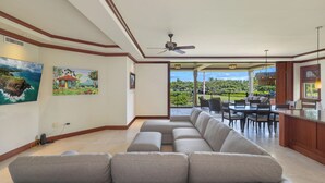 A spacious living room with a large gray sectional sofa, a ceiling fan, and a dining area with a table and chairs. - Kolea 2E -Newly furnished in 2024 3 BR Condo -Hilton Waikoloa Access Included (Waikoloa)