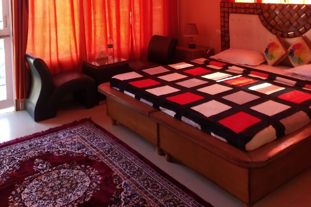 Una camera da letto con un letto grande, un ventilatore a soffitto, tende rosse, un tappeto decorato e un comodino con una lampada.